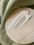 White bar of soap on a beige stone surface with green fabric in the background Macro of after-sun lotion smear with a translucent gel strip on a white marble plate, sage-green cloth draped along the edge.
