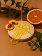 Honey being drizzled onto a plate with peaches and an orange on a brown background Peachy-grapefruit shampoo streaming onto flat stone plate with dried citrus fresh haircare scene