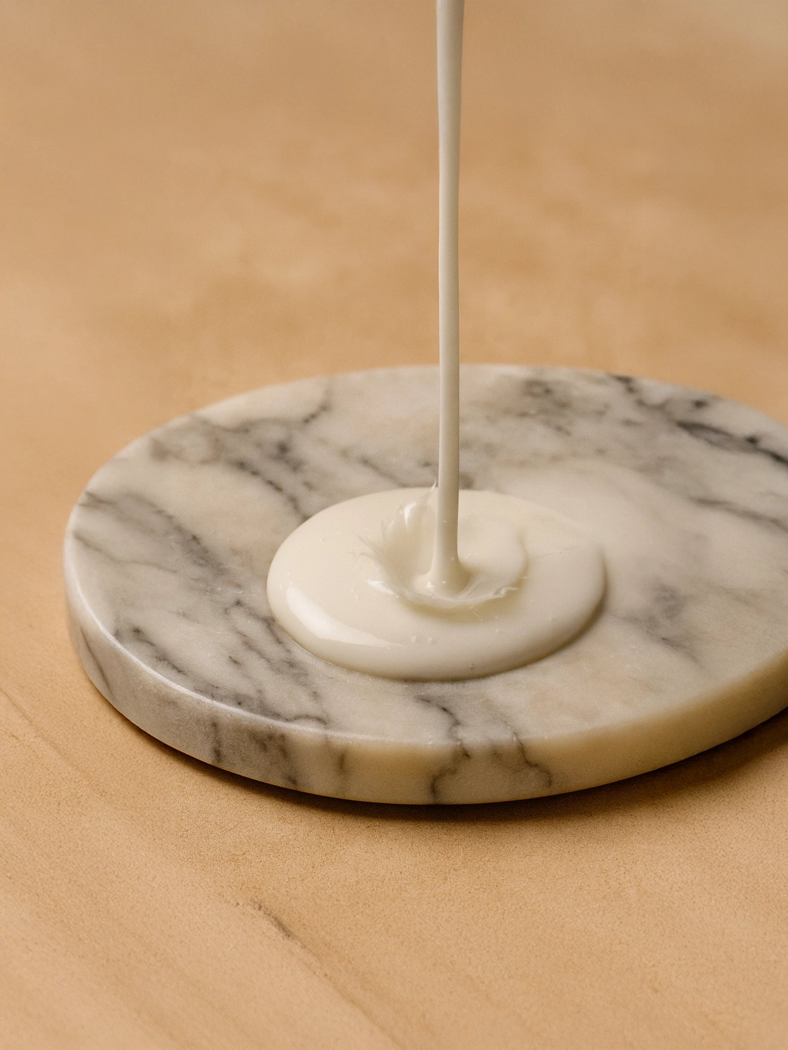 White liquid being poured onto a marble coaster on a beige surface Creamy white conditioner splashing on a dark marble plate with soft smoky lighting and earthy vetiver tones, capturing a luxurious spa-like atmosphere.