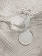 Clear glass with a white powdery substance on a textured beige surface Purifying Toner
