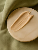 Beige cream on a round beige plate with a green fabric background Sunscreen SPF30, with tint