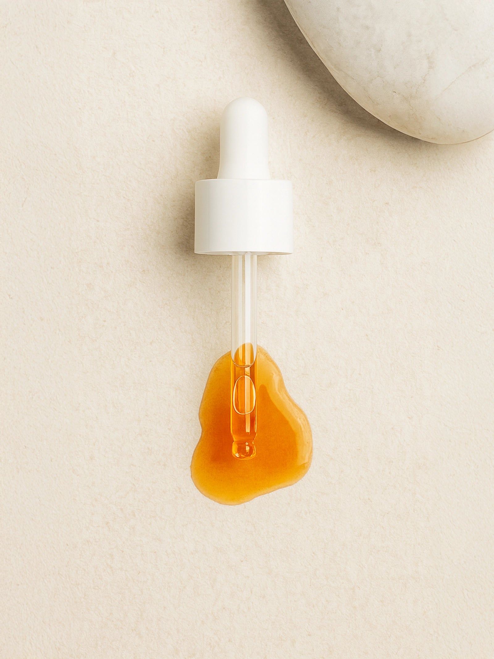 White dropper with amber liquid on a beige background