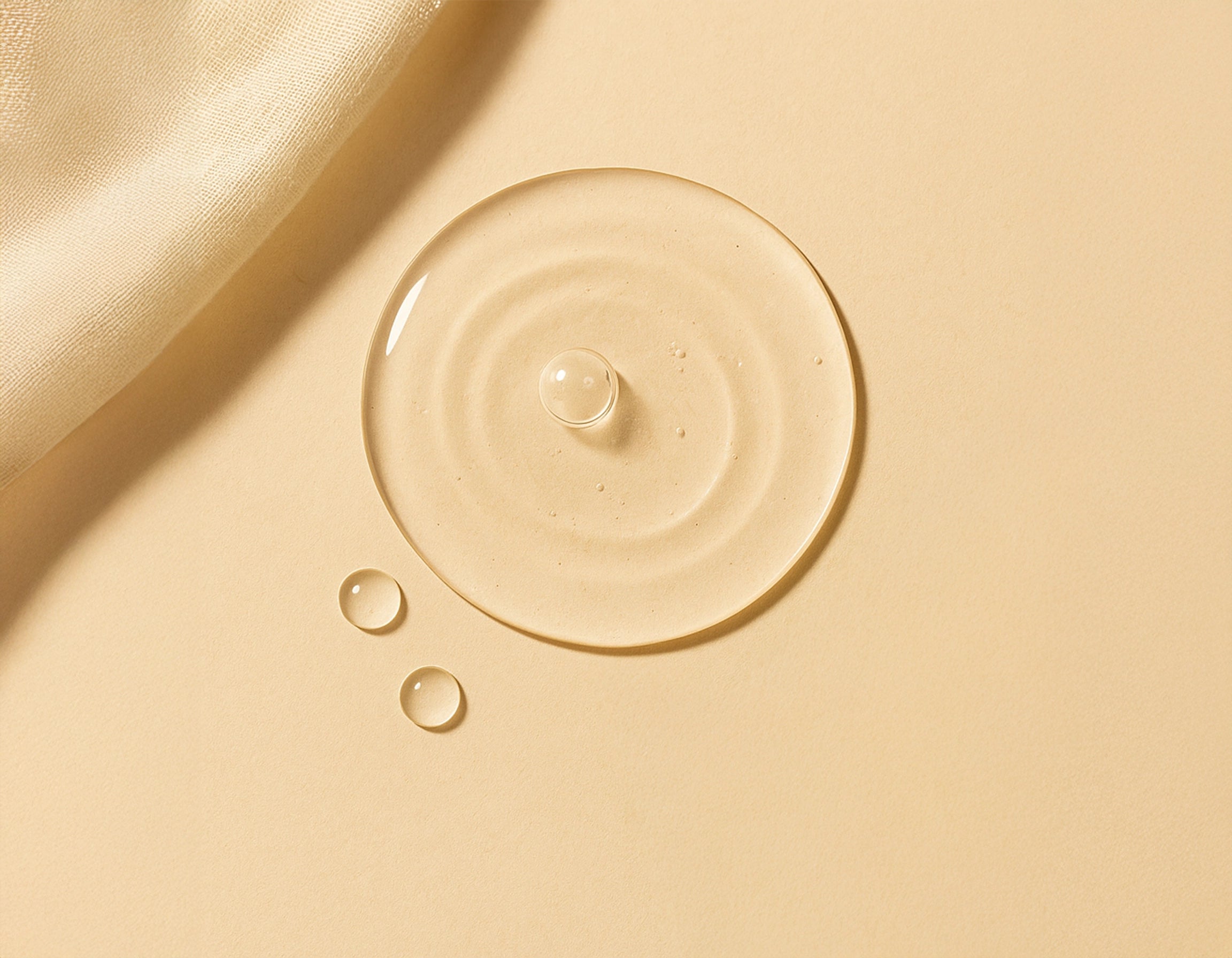 A clear droplet of hyaluronic acid resting on a warm beige surface beside aloe leaves, symbolizing deep hydration and purity – Suvera Self Care