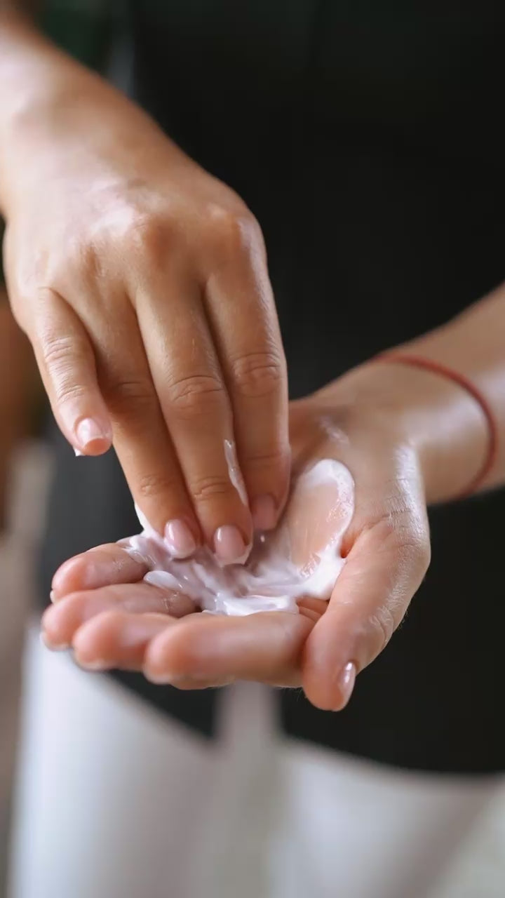 Moody product shot—glossy urea–panthenol cream swipe on black veined stone with green thyme accents.
