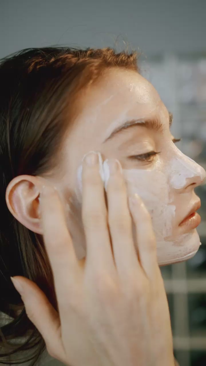 Close-up white pump beneath marble tile; clear gel droplet and soft bubbles on light beige fabric—clean, airy styling for sensitive cleanser.