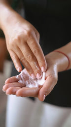 Close-up creamy stripe of soothing after-sun on round veined marble; soft green fabric half covers the plate.