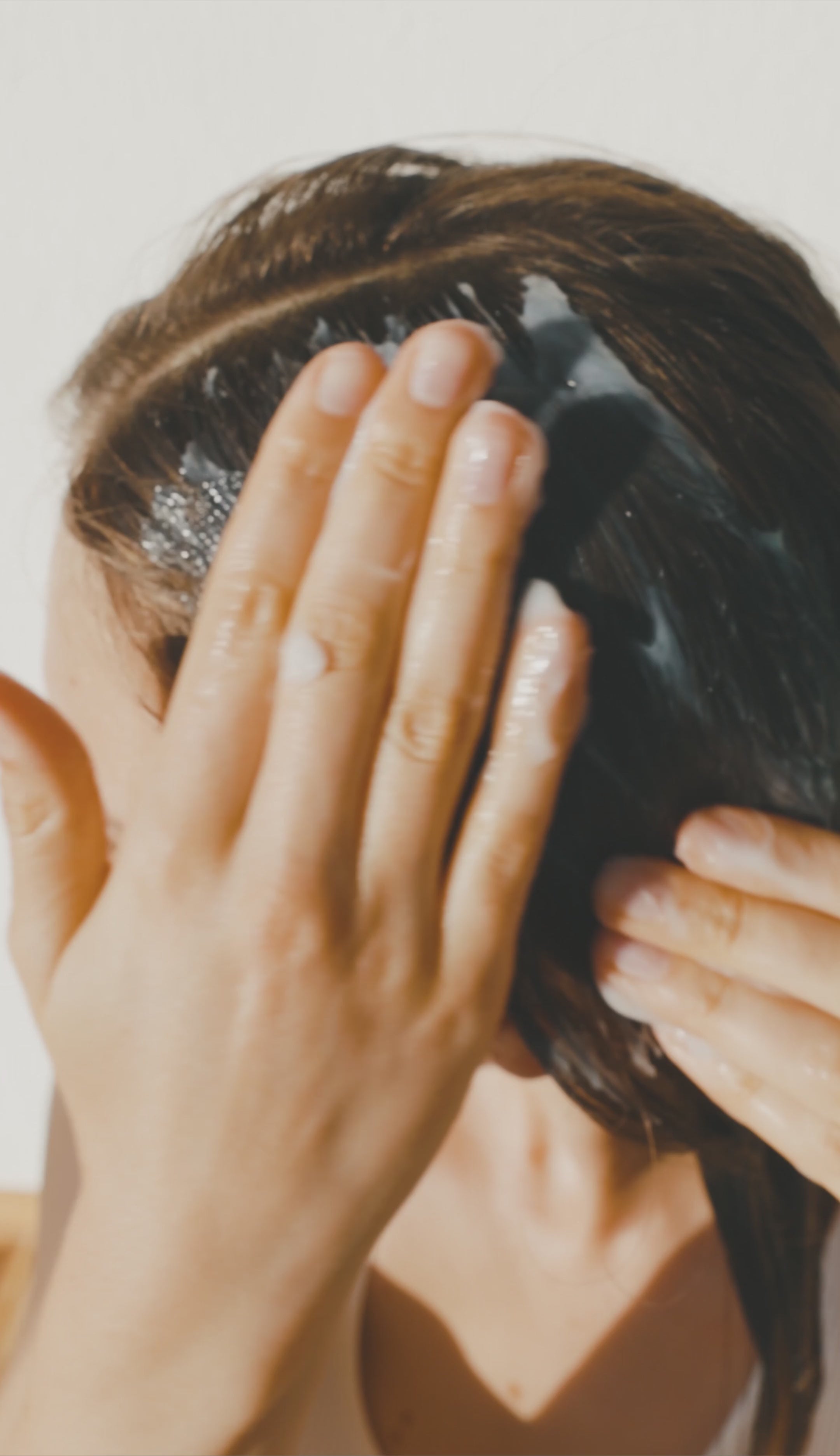 Glossy white conditioner drop on polished black marble surrounded by misty shadows and warm vetiver-inspired textures, emphasizing natural shine and depth.