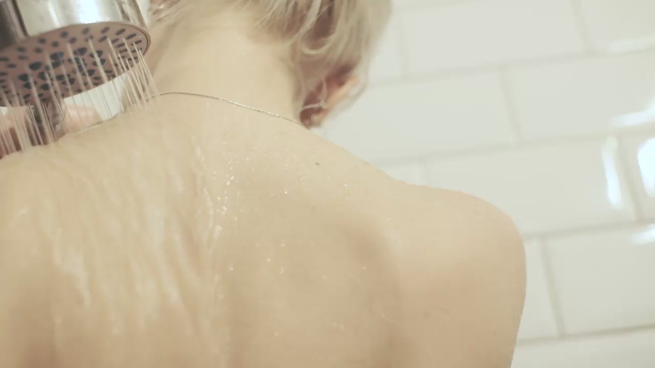 Smear of sensitive scalp shampoo on a clear glass tray over linen, framed by white lilies; overhead view.